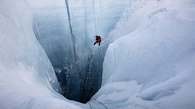 A figure descends by rope into a huge hole in the ice