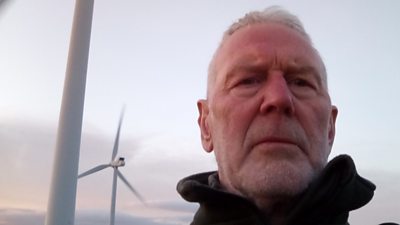 Mike Padgett stands unsmiling in front of a wind farm on this outskirts of his village of Sancton, in East Yorkshire.