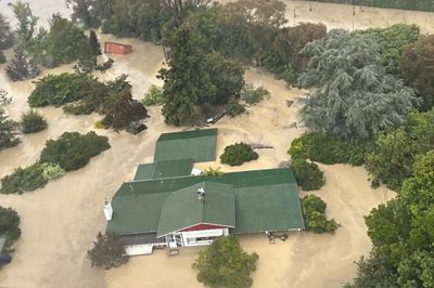 People stand on the rooftops of houses submerged in flood water