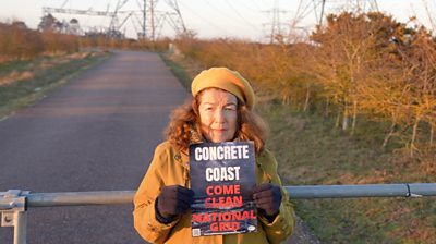 Campaigner Fiona Gilmore holds up a placard reading 'Concrete Coast: Come Clean National Grid'.