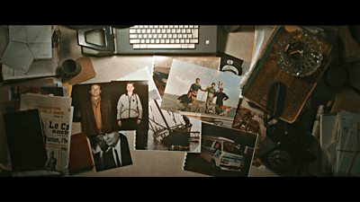 A desk top covered in vintage photographs with a typewriter and other props. 