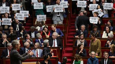Members of the French parliament hold placards and sing the Marseillaise