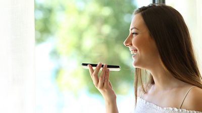 A woman is holding a phone in front of her mouth and is speaking into it.