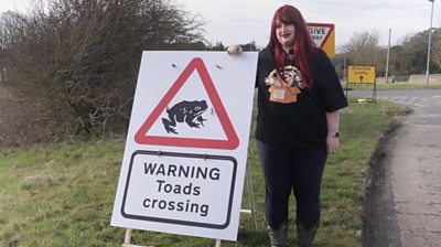 Hayley, aka 'Toad Girl', stood beside a toad crossing sign in Hexham
