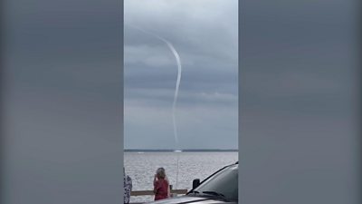 Waterspout stretches from lake to sky as people watch