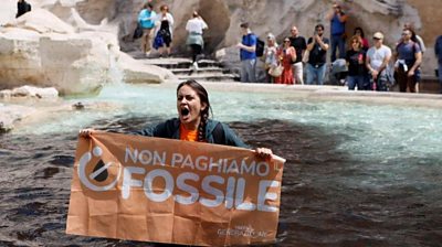 A climate activist holds a banner in Trevi Fountain, surrounded by vegetable charcoal that was poured in the water
