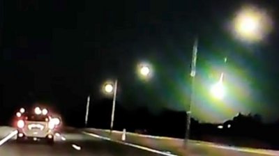 Green light flashes in dark sky above cars on road