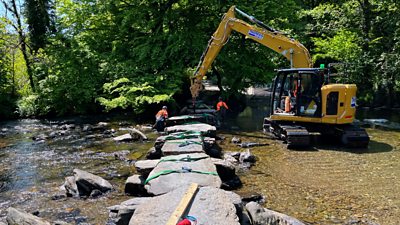 Workers use an excavator to put the stones back on Tarr Steps