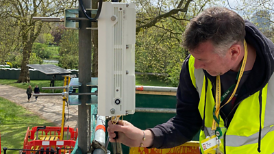 A man fixes a small mast on a scaffold