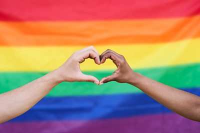two hands making a heart in front of a pride flag
