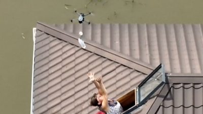 Drone drops a water bottle to a woman reaching for it from a skylight.