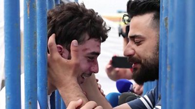 Two men smiling and embrace, with two rows of fences separating them