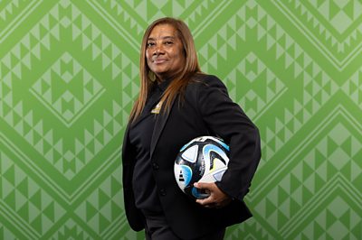 Desiree Ellis poses for official photo in suit and football tucked under one arm