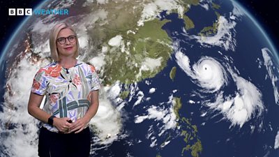 Sarah Keith-Lucas in front of a satellite weather map of Asia, showing Typhoon Khanun