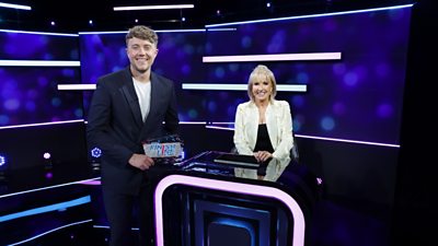 Roman Kemp and Sarah Greene standing at a podium with blue lights behind them