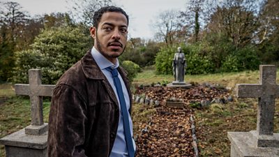 Daryl McCormack as Detective Colman Akande. He stands in a graveyard.