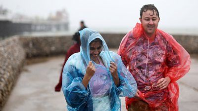 People walk in the rain along the sea wall next to the Palace Pier in Brighton, southern England on 5 August 2023