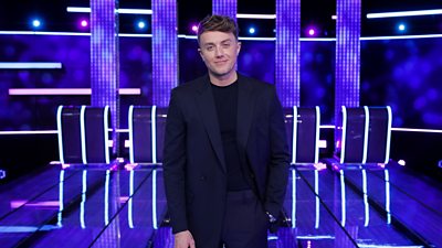 Roman Kemp standing in a studio with a navy suit
