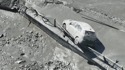 Car covered in mud hangs on railing