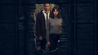 A man and a woman look through a hold in a wall