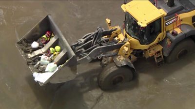 Residents carried in the front of a construction vehicle