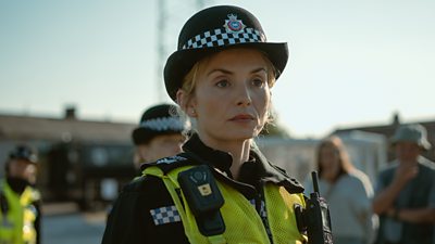 Sophie Melville as Thea - she stands outside in a police officer's uniform