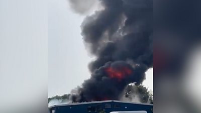 Video shows a large, black plume of smoke and flames rising from the site of a fire at a commercial building..