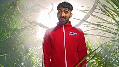 Mawaan Rizwan standing in a jungle backdrop with a red tracksuit