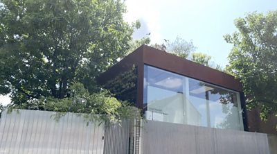 Cube-shaped ouse surrounded by trees behind a fence