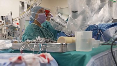 Robot arms next to surgery team in an operating theatre performing surgery