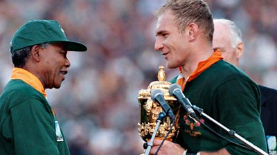 Nelson Mandela presents Francois Pienaar with the Rugby World Cup trophy in 1995, both wearing Springbok jerseys