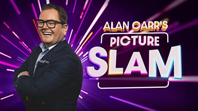 Alan Carr stands side on with his arms folded wearing a dark suit, blue shirt. He's wearing large dark rimmed glasses and smiling. Alan Carrr's Picture Slam is written in multicoloured graphics beside him. 