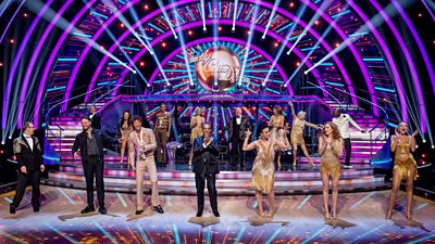 The Strictly Come Dancing celebrities line up on the ballroom floor in glittering gold and black costumes, waiting to meet their professional partners