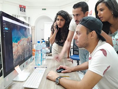 Two young men and two young women cluster around a computer screen