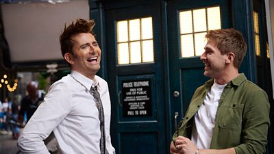 David Tennant and Steffan Powell stand outside the Tardis on location laughing together for Doctor Who Unleashed