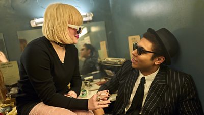 Jeannie Keefe played by Eve Austin and Dante Williams played by Levi Brown. Jeannie is sitting looking down at Dante with a cigarette and sunglasses on. Dante is looking up to her with sunglasses on