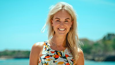 Survivor contestant Ashleigh stands on the beach wearing a multicoloured leaf patterned top, smiling for the camera