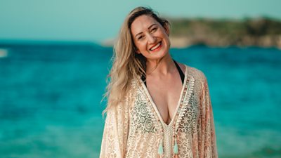 Survivor contestant Jess stands on the beach wearing a tasseled beach dress over a two piece swim set