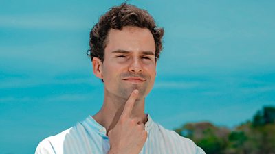 Survivor contestant Laurence stands on the beach wearing a white shirt