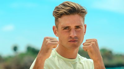 Survivor contestant Lee is pictured on the beach wearing a lime t-shirt and holding both fists up as if ready to fight