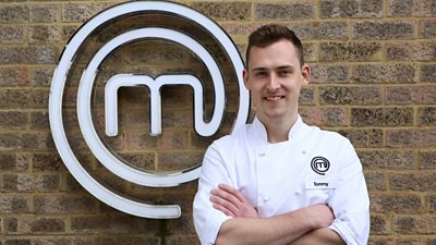 Man wearing chefs clothing smiling in front of MasterChef M