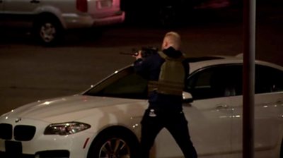 Armed police officer with a gun, behind a car