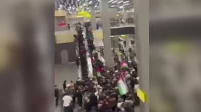People storming inside of airport, taking escalators an waving Palestinian flags