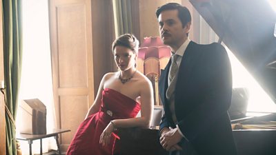 Character Bridget wearing a red evening dress beside Lord Whitfield wearing a suit both leaning on piano