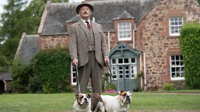 man wearing tweed suit and hat outside stately home with two english bulldogs