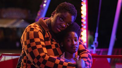 Image featuring Déborah Lukumuena and Le’Shantey Bonsu in Girl. The pair embrace on a fairground ride.