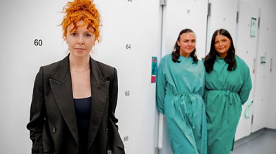 Stacey Dooley stands in front of two women wearing green protective clothing