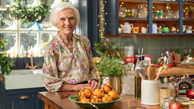 Dame Mary Berry stands at the counter in a festively decorated kitchen, smiling