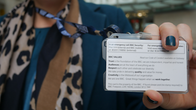 A BBC journalist holding their ID badge where the BBC values are written.