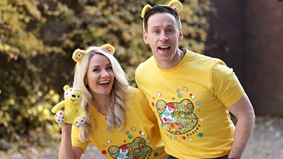 Holly Hamilton and Connor Philips smile to the camera wearing yellow BBC Children in Need t-shirts and Pudsey headbands. 